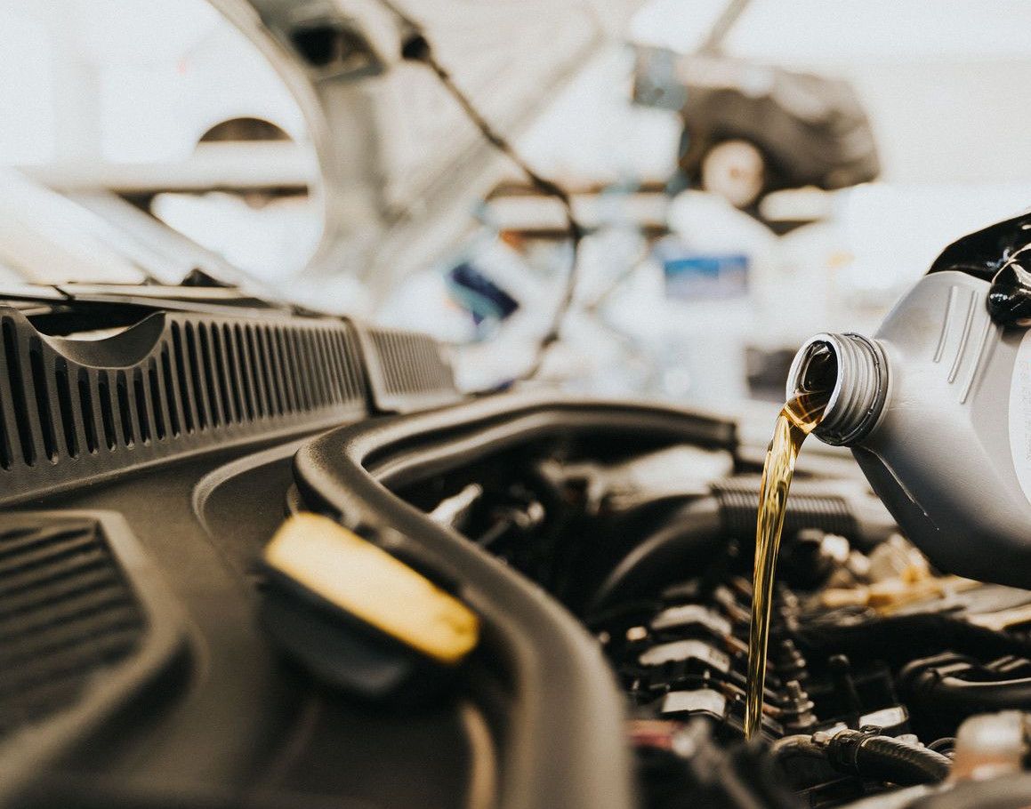 Close-up of a mechanic pouring engine oil into a car engine in an auto repair shop.