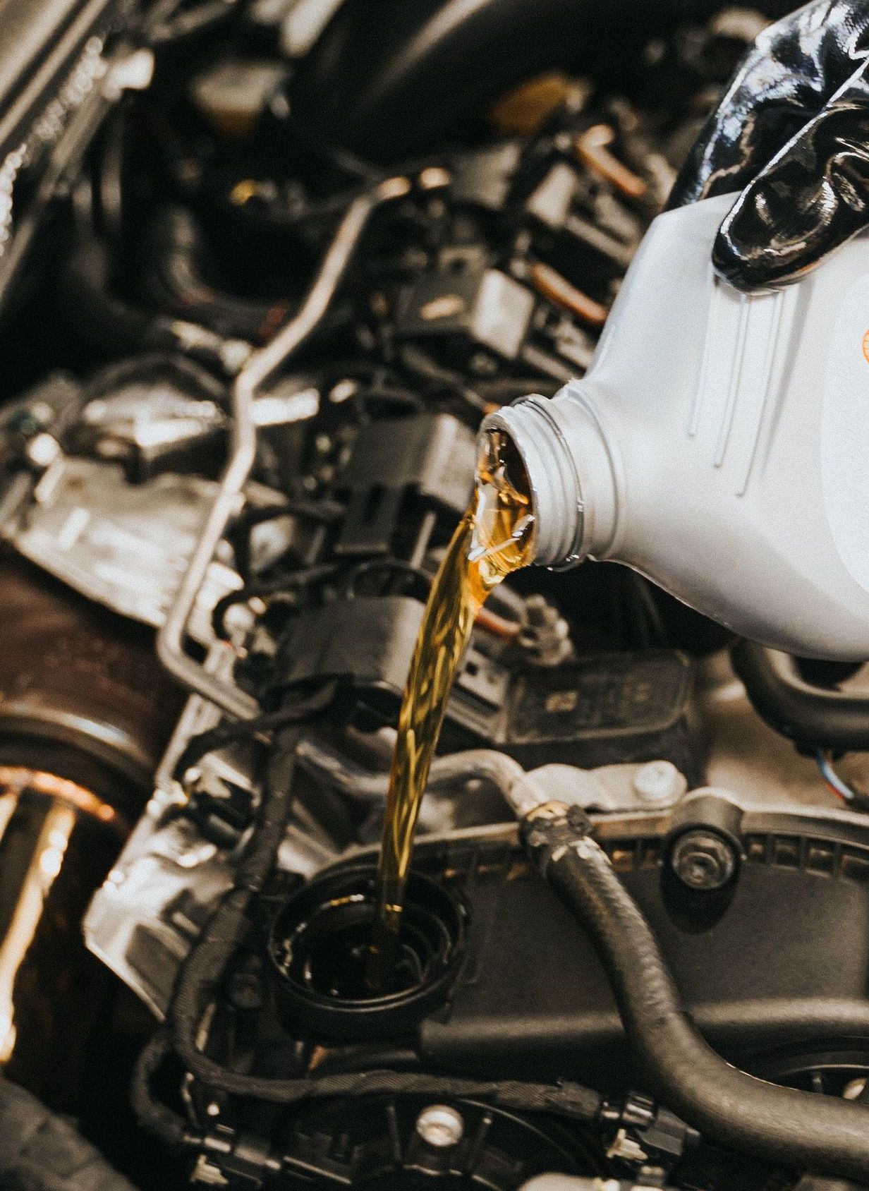 Close-up of mechanic pouring engine oil into car engine with gloved hands, showcasing automotive maintenance.